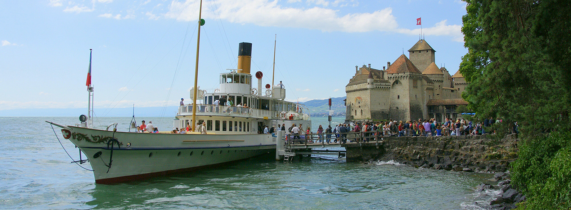CGN sightseeing ferry moored at Chillon Castle on Lake Geneva, with visitors boarding and the historic Swiss castle in the background.