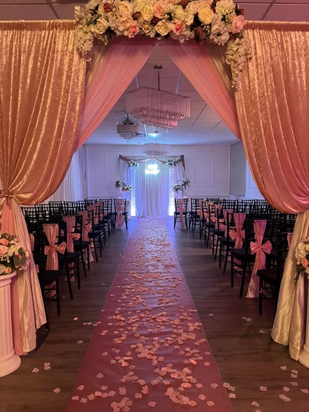 Enchanting pink ceremony space adorned with delicate pink flowers on the ground, featuring an entrance embellished with pink curtains and captivating pink and cream flower arrangements at The Palmyra Venue in New Jersey