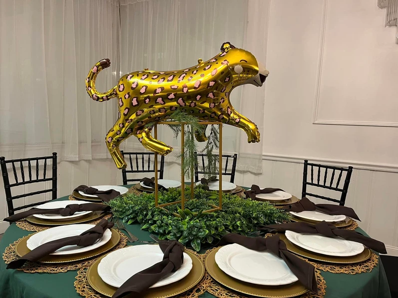 Round table adorned with a green tablecloth and a brown napkin, leopard balloon centerpiece at The Palmyra Venue.