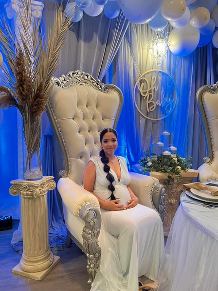 "Expectant woman sitting on a chair amidst light blue and gray themed decorations, celebrating a joyous baby shower at The Palmyra Venue