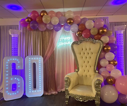 Luxurious cream-colored chair adorned with elegant pink and gold decorations, accompanied by illuminated number 60 and surrounded by stunning pink-toned floral arrangements at The Palmyra Venue.