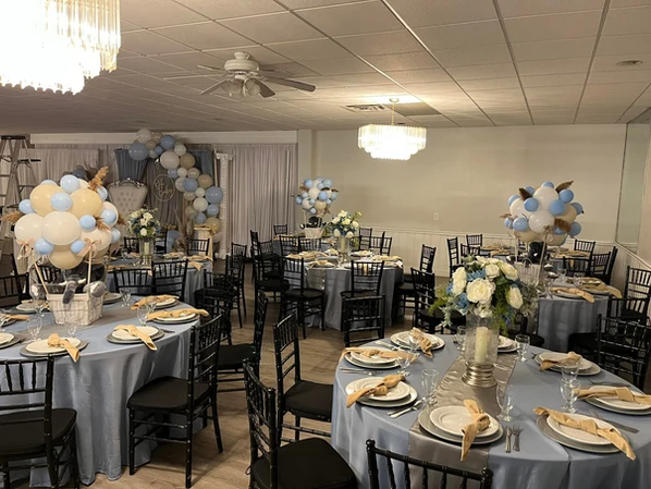 Round tables adorned with light blue and gray themed decorations for a baby shower, showcasing beautiful floral centerpieces amidst a sea of balloons at The Palmyra Venue.