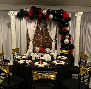 Round black tables adorned with red, gold, and black themed decorations and balloons for the event at The Palmyra Venue, New Jersey