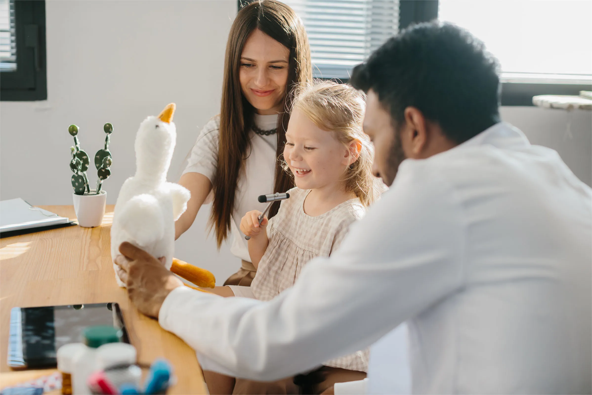 педиатър, показвайки играчка гъска на дете и майка му