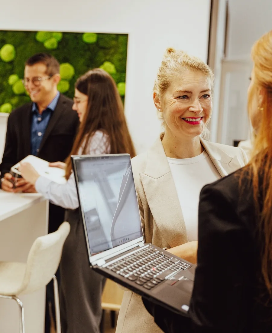 Two women talking with a laptop with foxdot employees in the background.