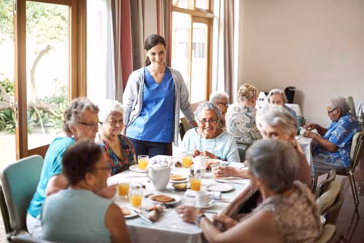 seniors at dining room table eating with staff watching