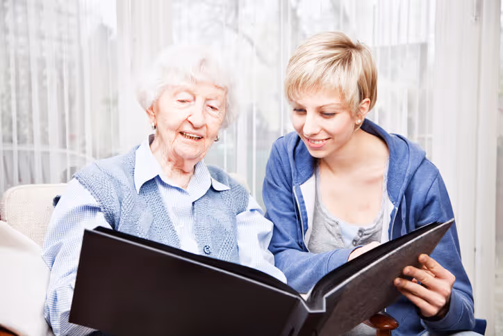 elderly woman and a young woman smiling as they look through a photo album together