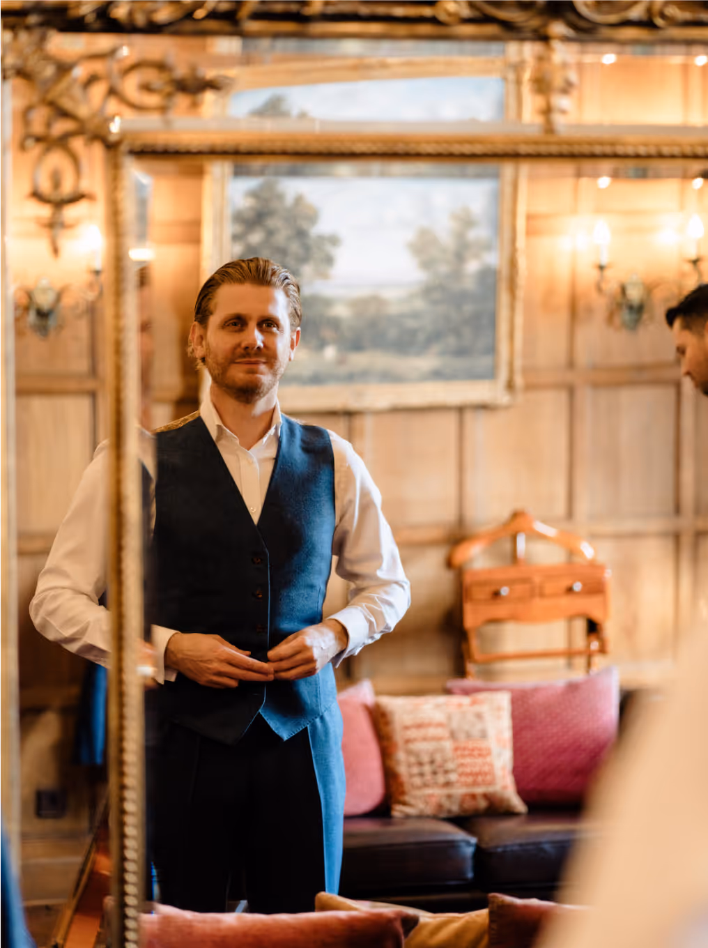Opulent groom's room in historic mansion, featuring oak paneling, vintage mirror, leather couch, and valet