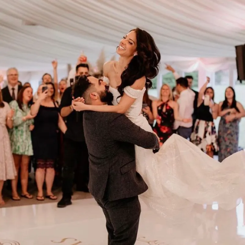 Euphoric bride and groom dancing with joy, embraced by their exuberant friends and family in our spacious pavilion. The groom lifts the bride in the air, capturing a moment of sheer celebration