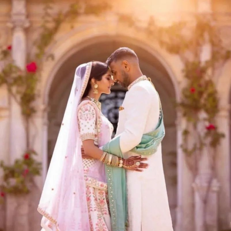 Embracing forehead to forehead, a blissful Asian couple holds each other closely during their country house wedding. The romantic Loggia serves as the backdrop, accentuating the intimate moment, while a sprinkle of vibrant red roses adds to the enchantment