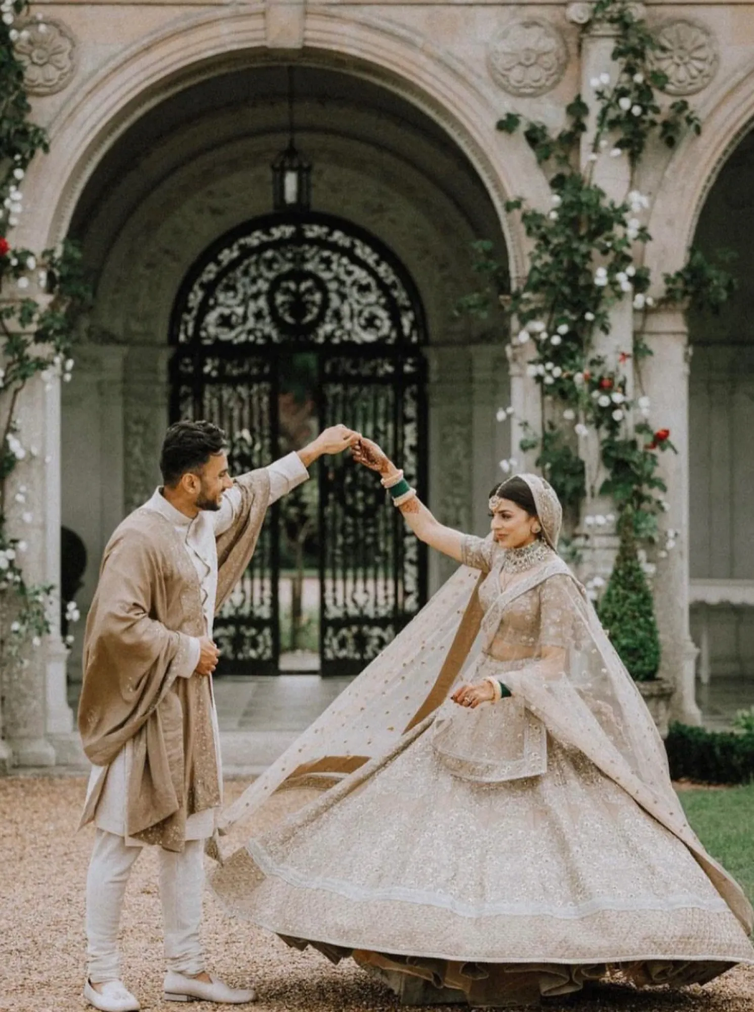Hand in hand, a joyful Indian couple, dressed in their traditional attire, spin with delight in front of the breathtaking Loggia, creating a captivating moment at their celebration