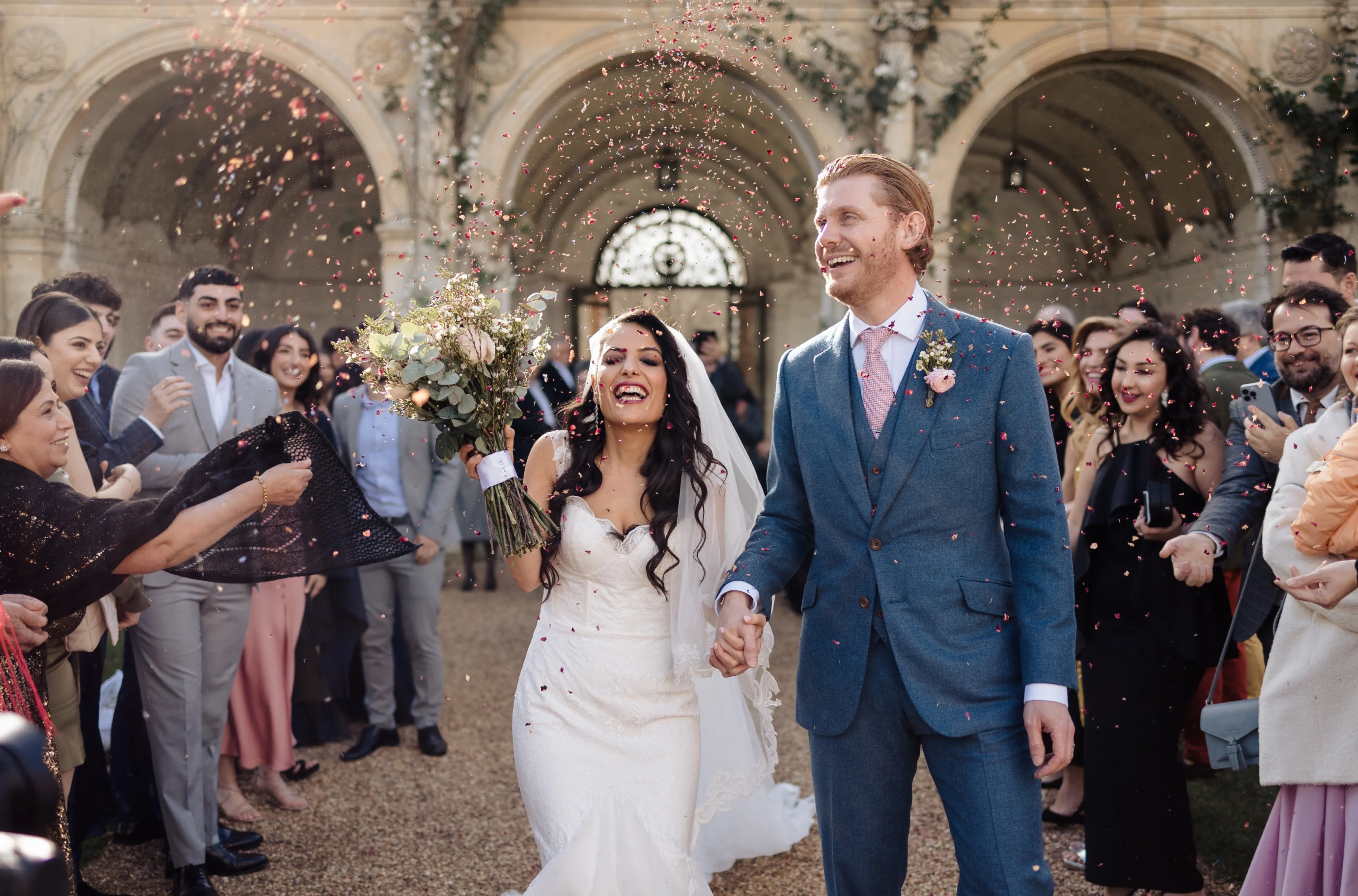 Newlyweds share joy after their civil ceremony at North Mymms Park's Loggia. Colorful confetti fills the air, capturing the happiness of their summer wedding amidst lush surroundings