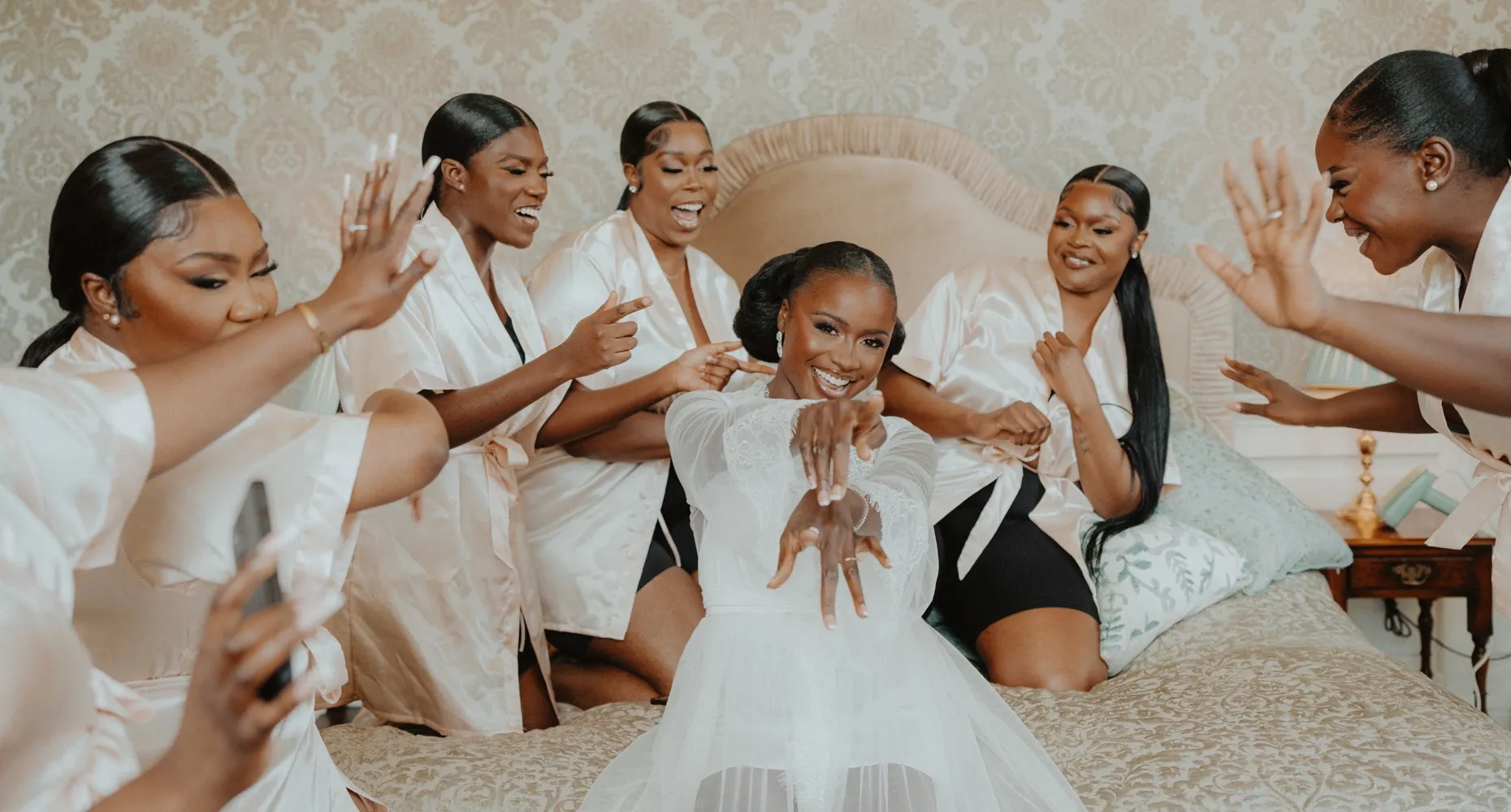 An ecstatic African bride and her elated bridesmaids having fun and dancing on the plush and luxurious bed in our lavishly adorned bridal suite at North Mymms Park. The spacious and opulent suite offers a perfect setting for the joyous celebration, with its elegant decor and comfortable ambiance. The bride and her bridesmaids create a lively and festive atmosphere, making the most of their special moments together before the wedding