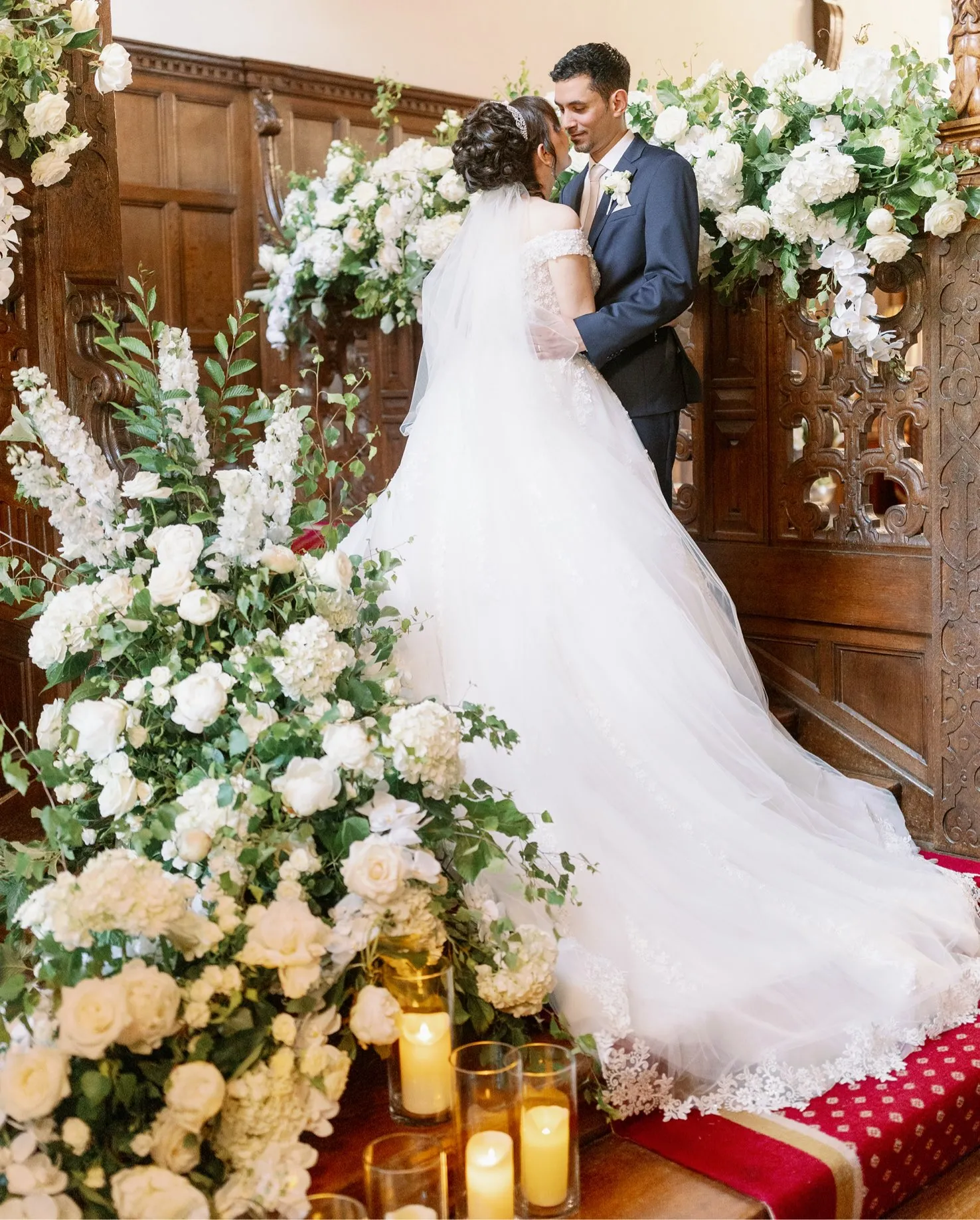 A picture-perfect moment captured at North Mymms Park. The newlyweds stand on a historic and elegant wooden staircase, gazing into each other's eyes. The staircase is adorned with an abundance of white flowers, adding a touch of timeless beauty to the scene. The combination of the historic setting and the delicate floral decorations creates a romantic and unforgettable moment for the happy couple on their special day
