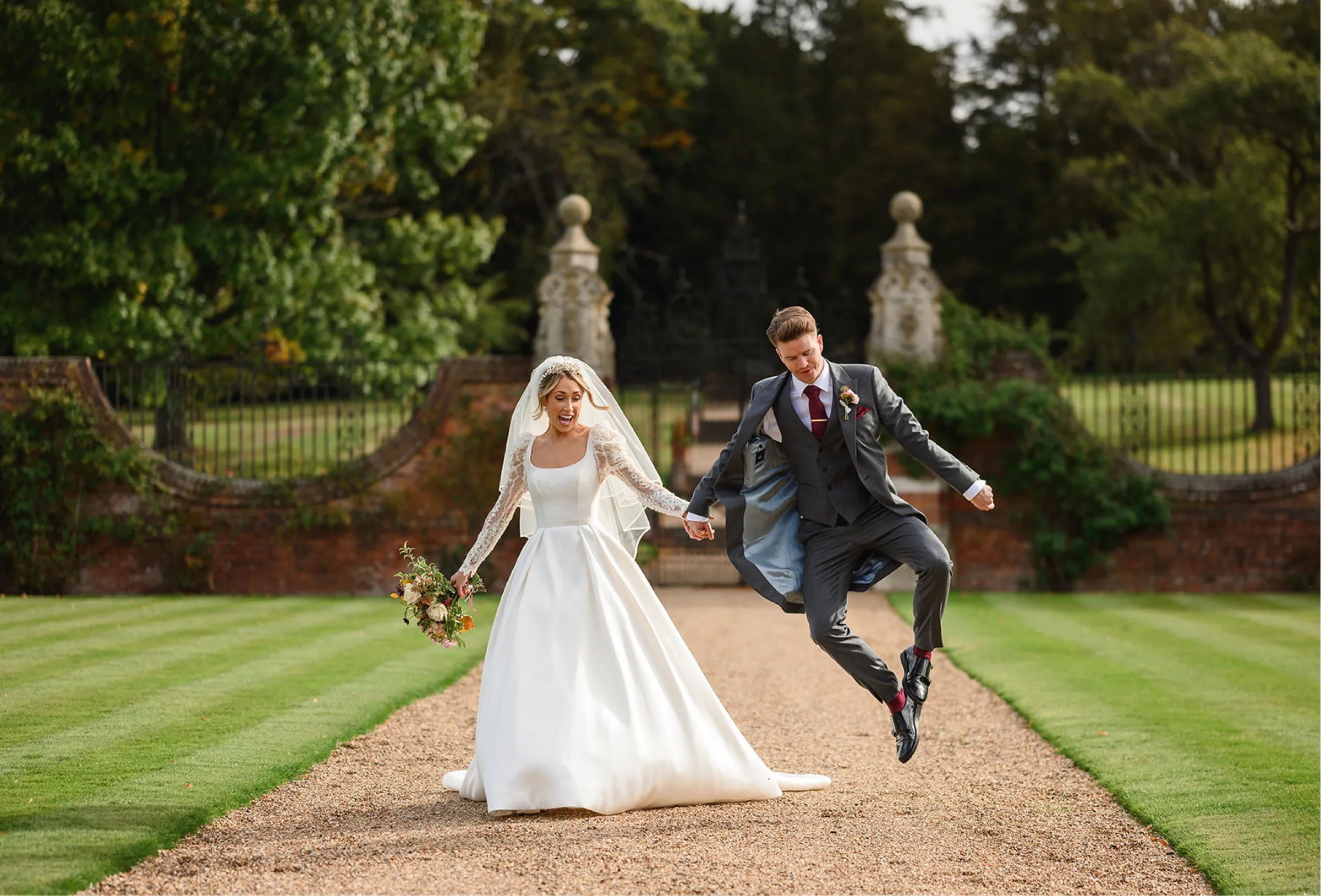 Overflowing with happiness, the bride and groom share laughter in the grounds of North Mymms Park during their luxury outdoor wedding. The groom's joyous jump adds to the celebration's exuberant atmosphere