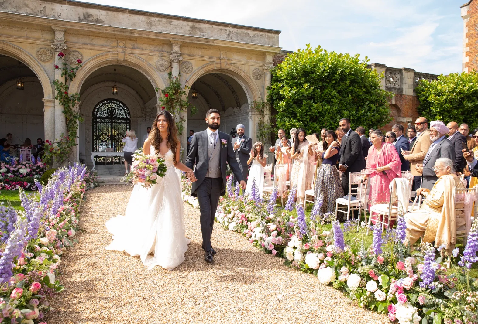 Romantic summer wedding with loggia and three marble arches. Newlyweds walk hand in hand down a flower aisle, surrounded by loved ones. Happiness and love under the setting sun