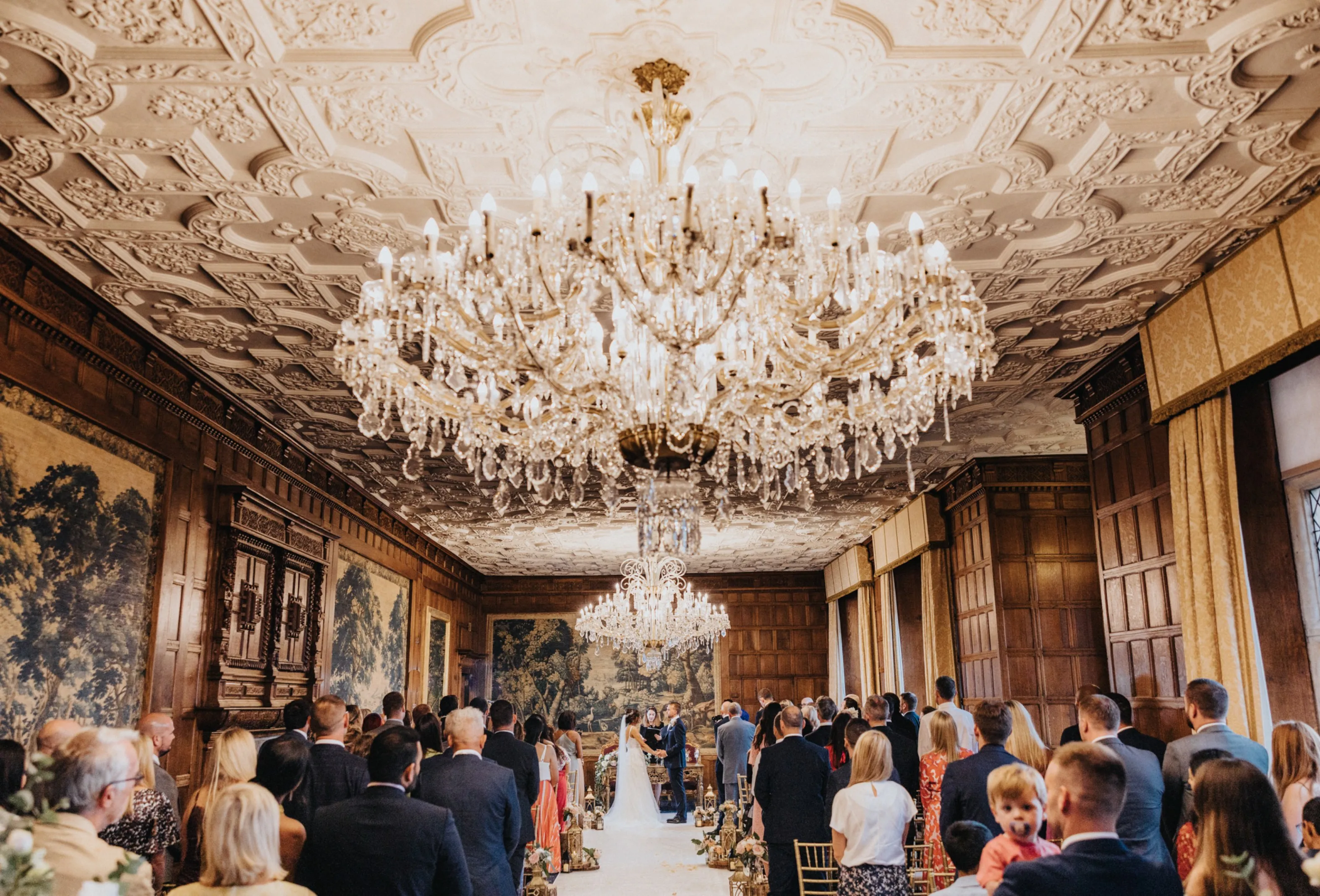 Magnificent Long Gallery with gold leaf mirrors, spectacular ornate ceiling, and stunning period windows. The chandeliers and verdure tapestries set the atmosphere of the Elizabethan era for a heartwarming civil wedding ceremony