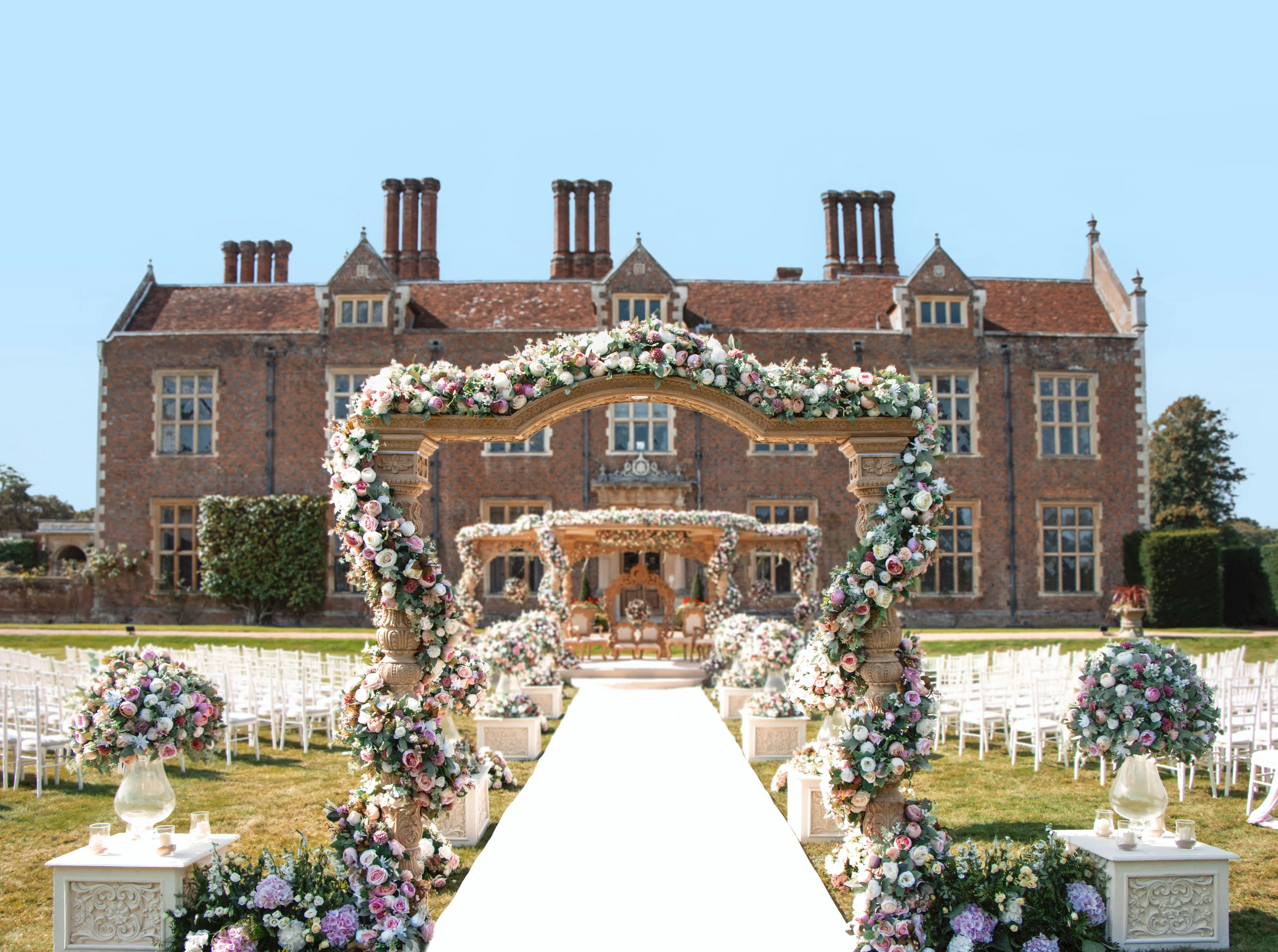 Captivating summer wedding at North Mymms Park, featuring a beautifully adorned mandap. The splendid mansion house in the background adds to the enchanting atmosphere of the celebration