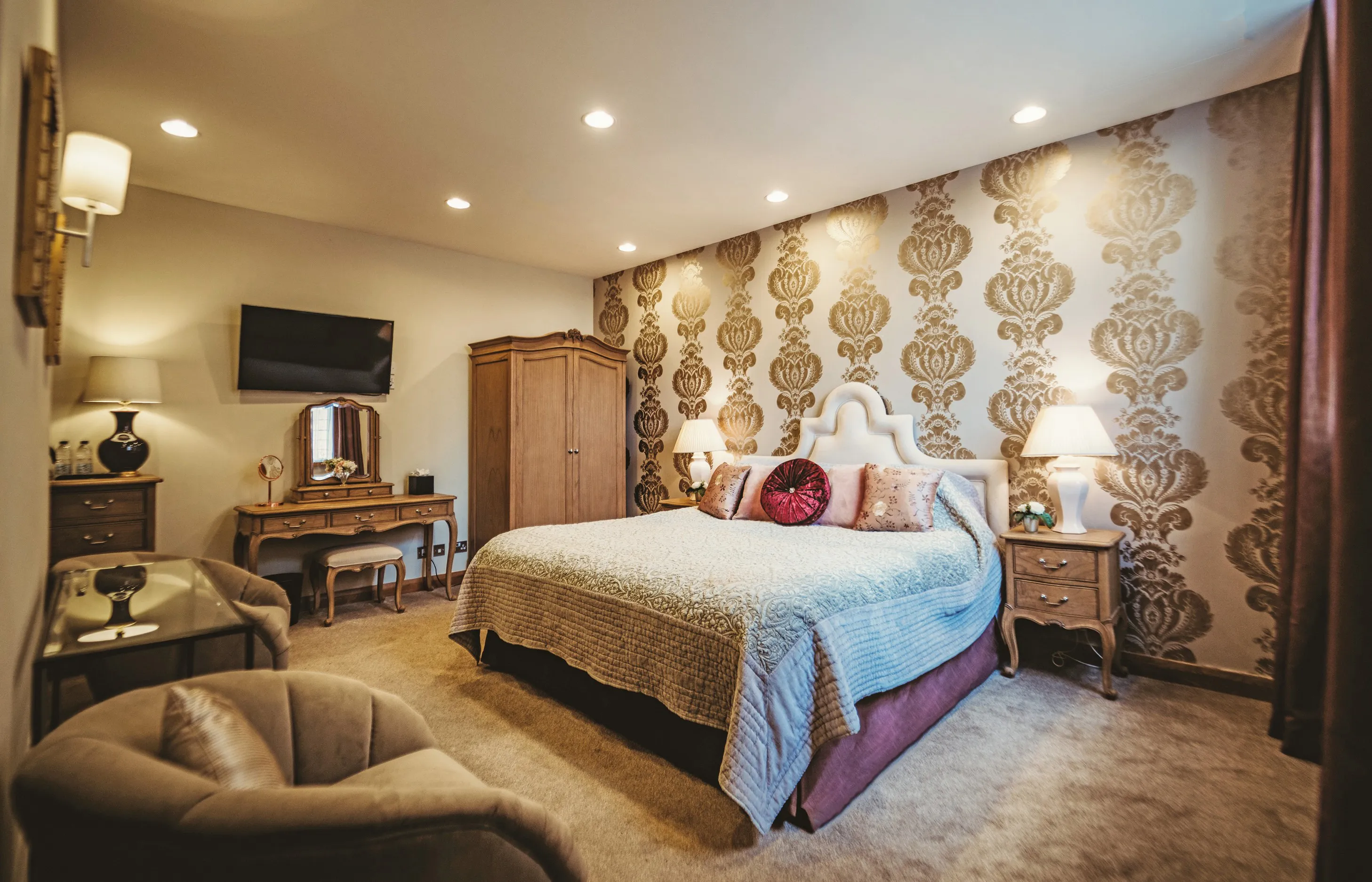 A luxurious bridal suite in the stables at North Mymms Park. The room features a grand king-sized bed, elegantly adorned with cushions, offering a regal and comfortable sleeping arrangement. The suite also includes a sleek TV, a spacious dressing table, and coffee facilities for added convenience. Large mirrors add a touch of opulence to the space, while an en-suite bathroom ensures a private and pampering experience for the bridal couple