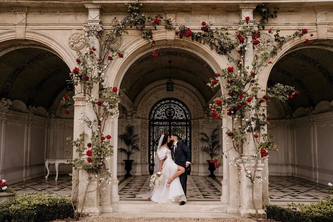 Romantic wedding setup - happy couple are kissing under the red rose arch