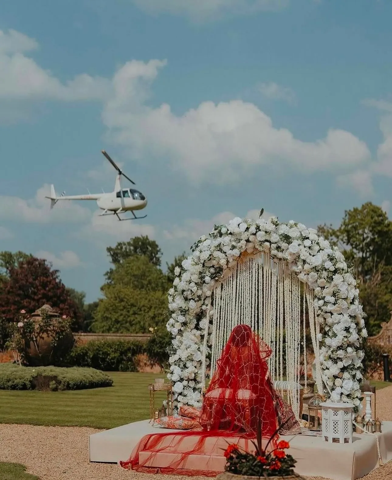 Radiant Muslim bride, dressed in her traditional outfit, waiting for her Nikkah ceremony in the scenic gardens of North Mymms Park. A helicopter can be seen in the background, bringing the groom to the venue, adding a unique and dramatic touch to the special moment.