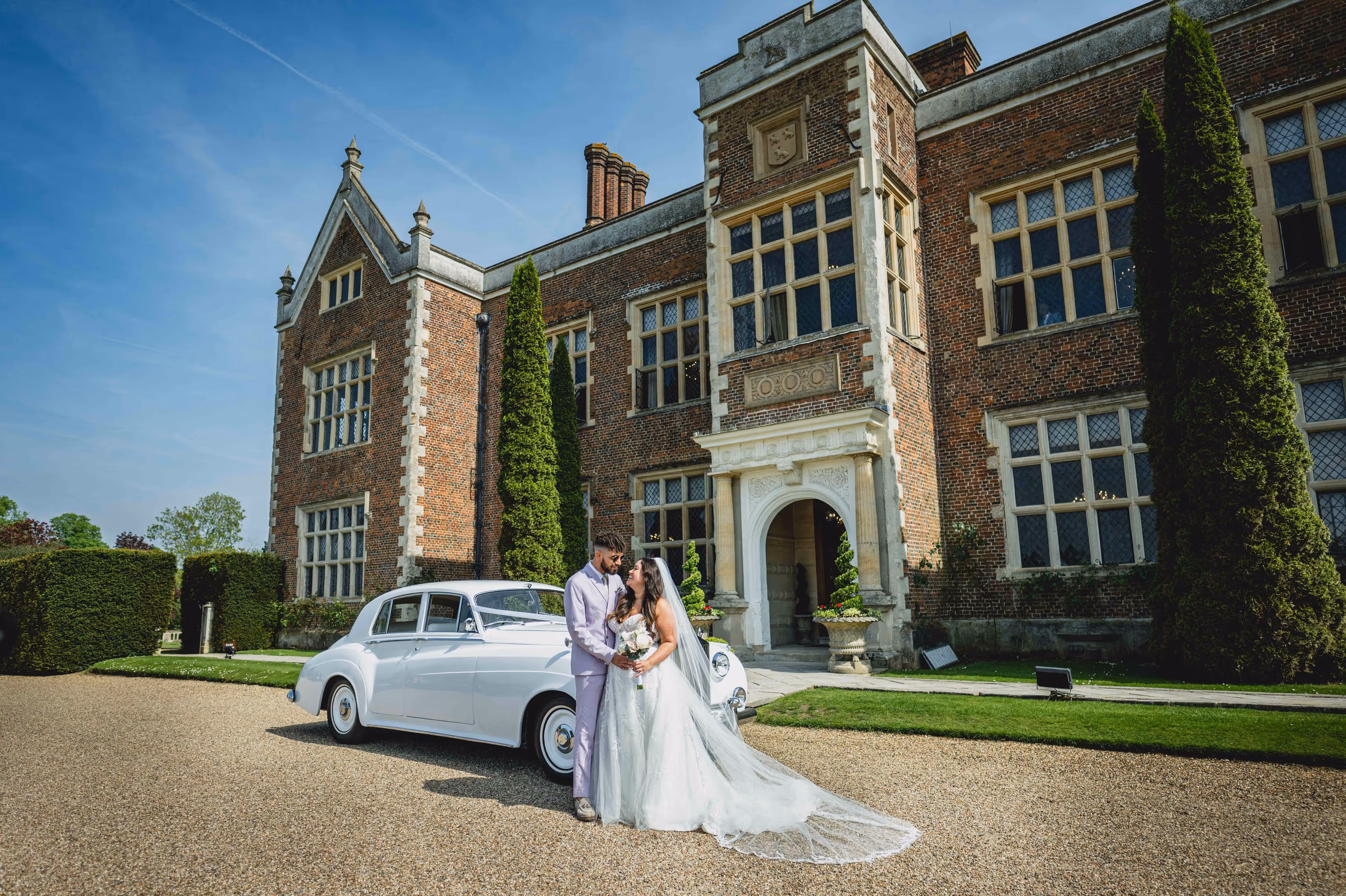 The bride and groom stand hand in hand in front of the stately Mansion House at North Mymms Park, framed by its historic architecture and lush surroundings.
