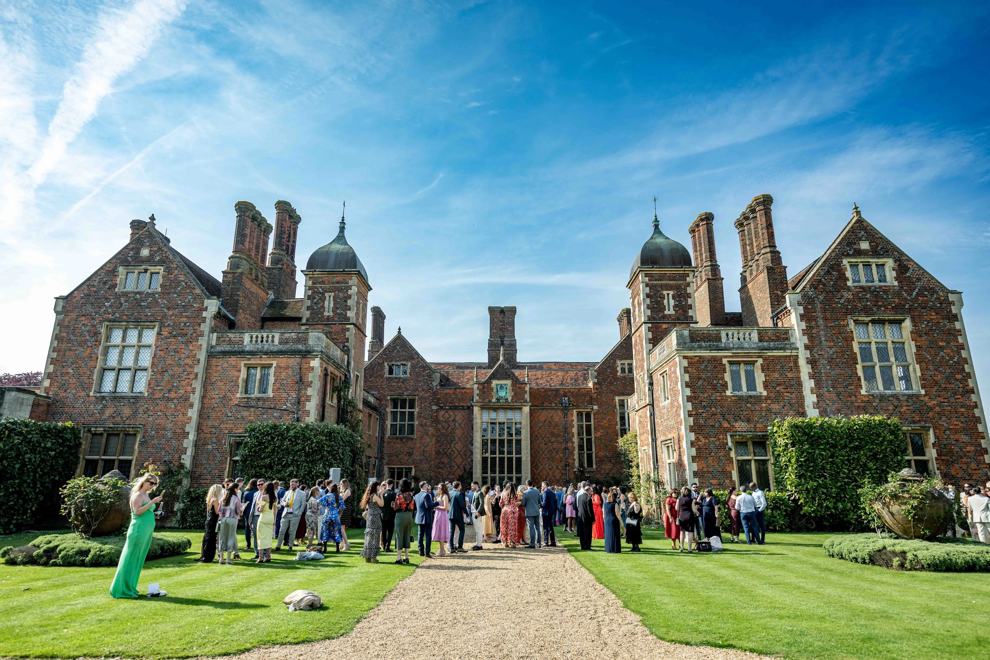 Guests enjoy a vibrant summer wedding in the lush gardens of North Mymms Park, with the stunning Mansion House providing a majestic backdrop.