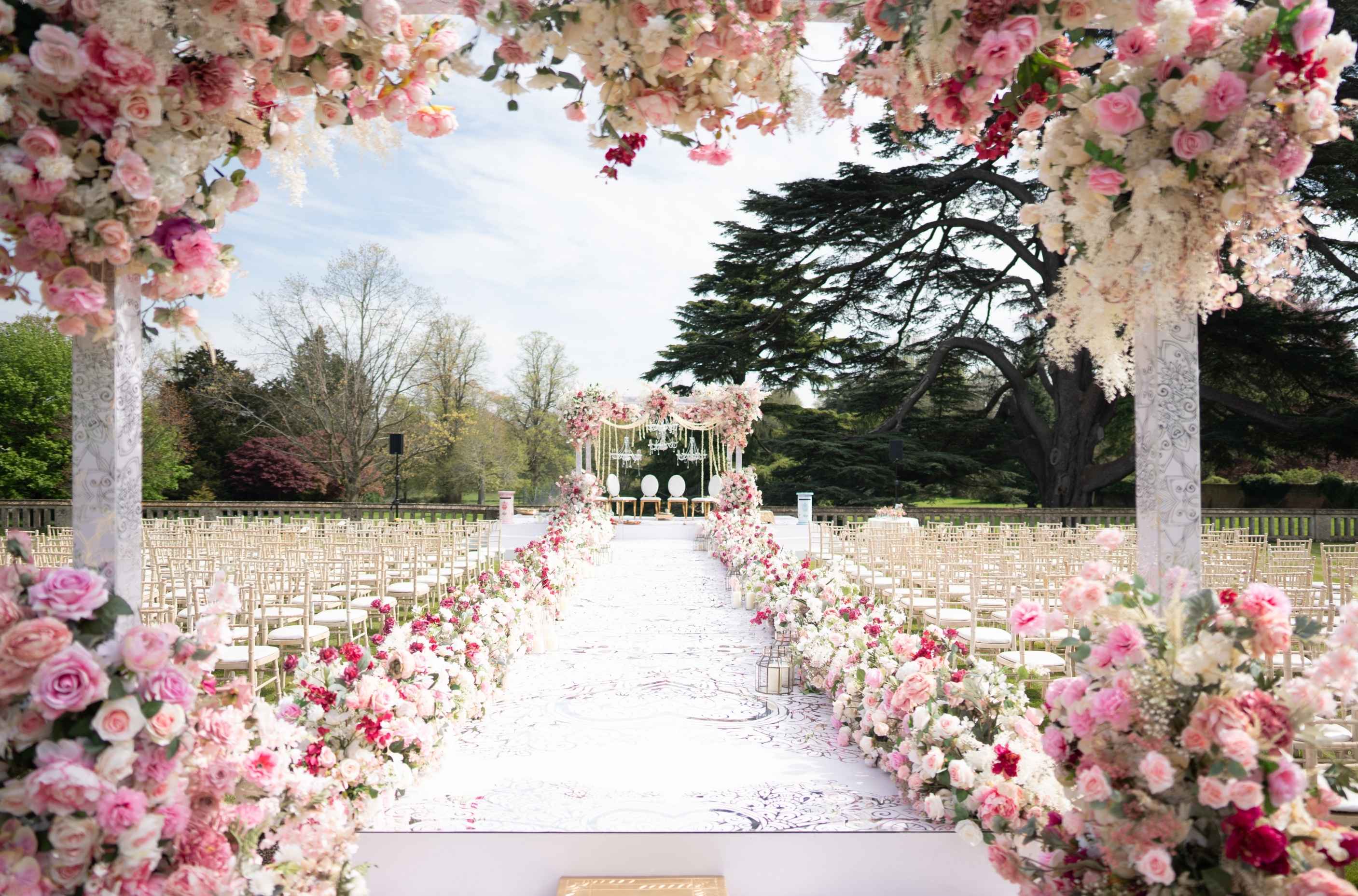A spectacular outdoor Hindu wedding ceremony setup at North Mymms Park, featuring a white aisle runner lined with pink and white flowers leading to a grand mandap.