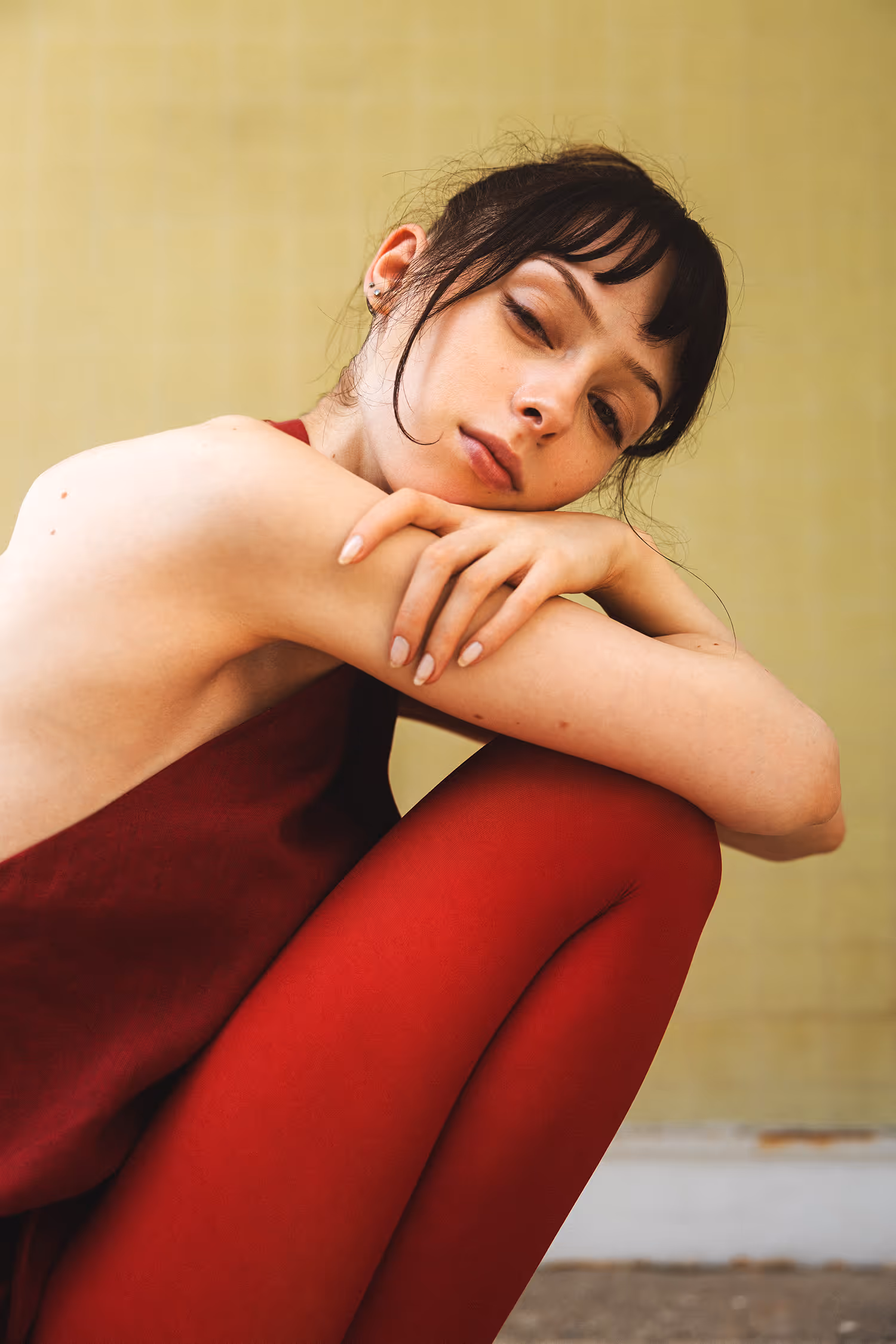 A woman dressed in red in a sensual pose against a yellow wall