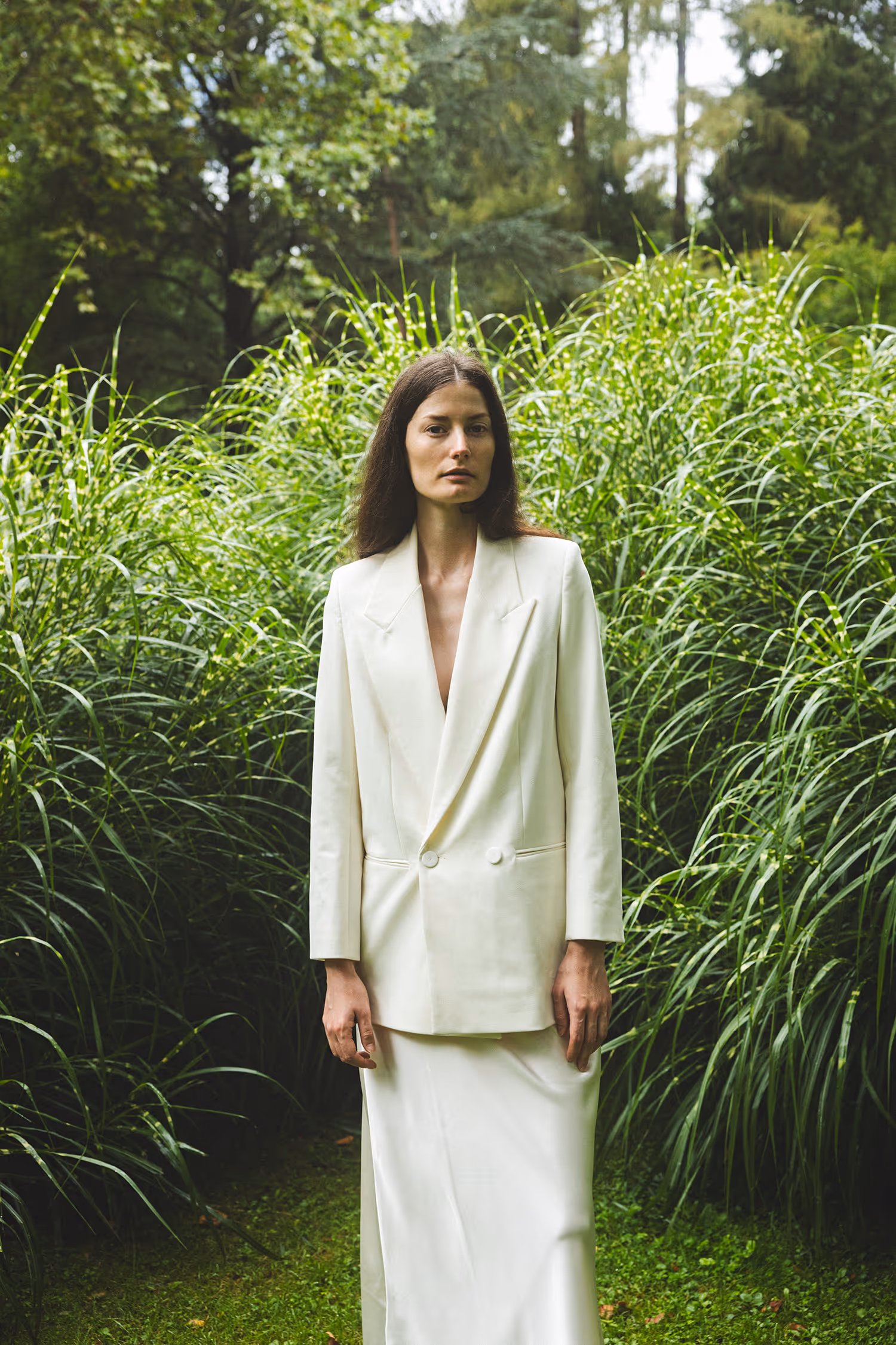A woman in a white blazer standing among tall grass
