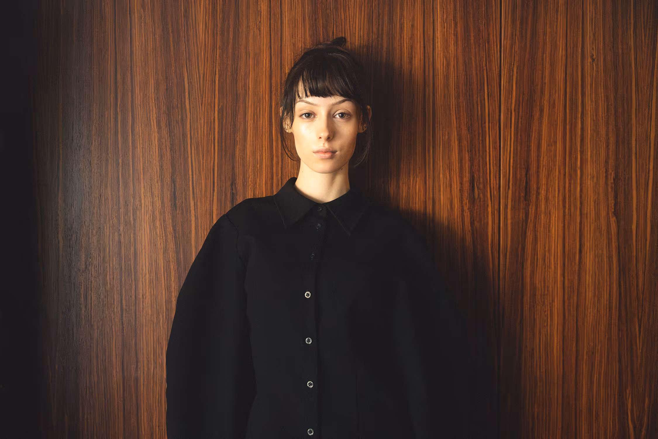 Woman in a black costume leaning against a wooden wall