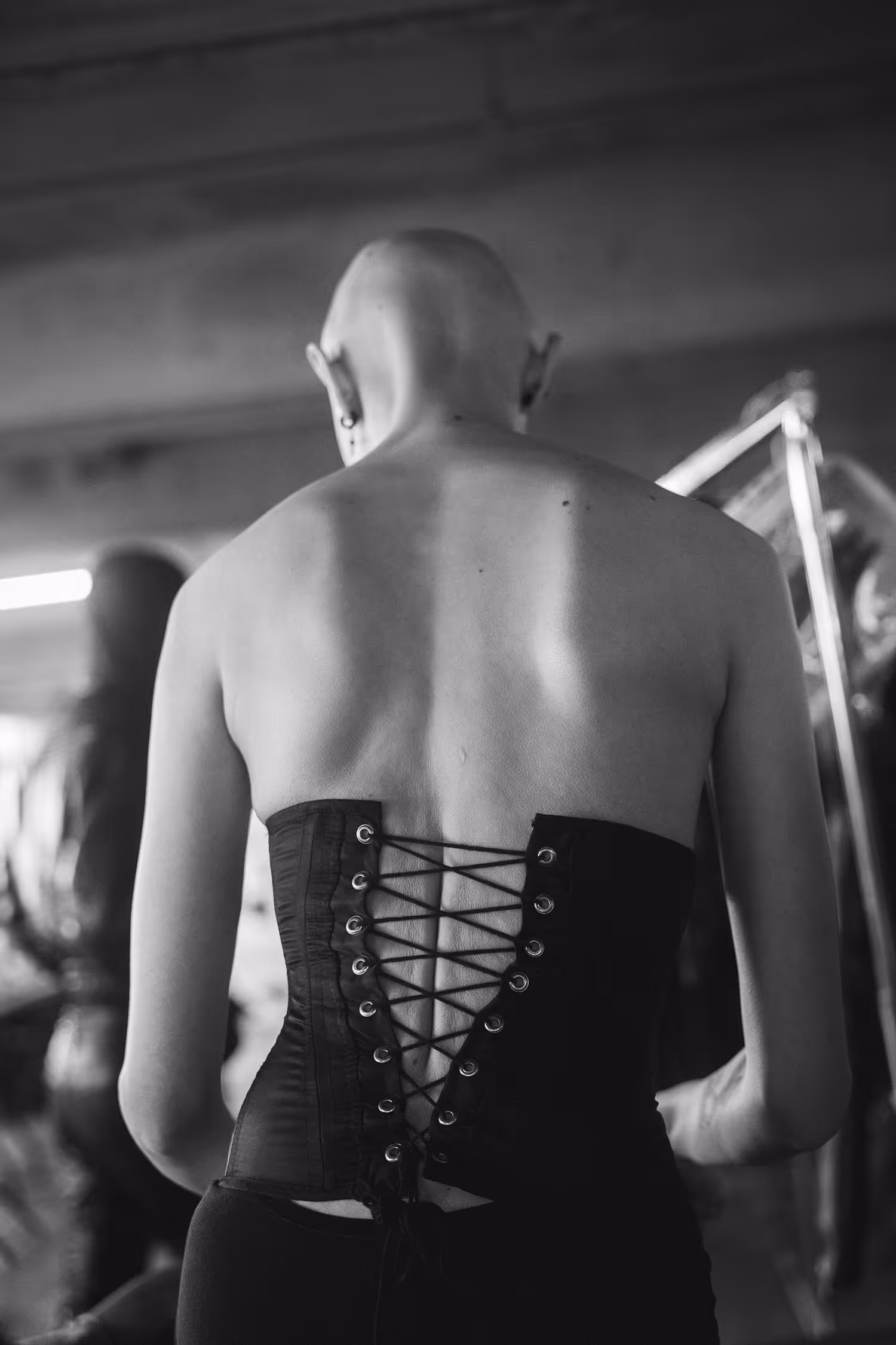 Bald model in a corset standing with her back to the camera