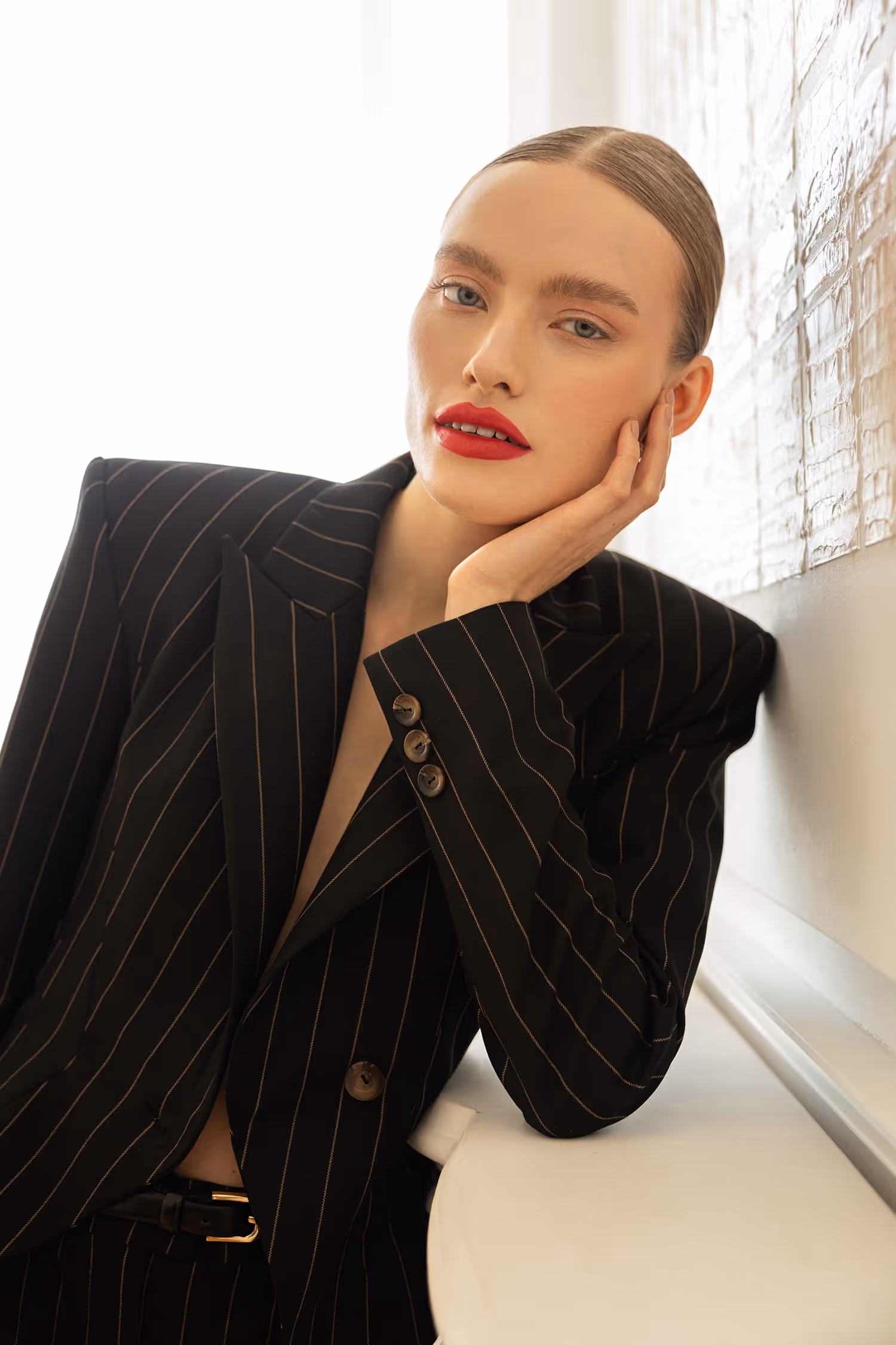 Bold fashion portrait in Warszawa, showcasing a model in a sharp pinstripe blazer with dramatic red lipstick and slicked-back hair, using soft directional light.