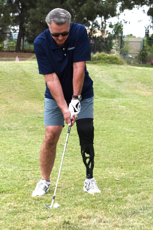 Man with a prosthetic leg preparing to hit a golf ball on a grassy course.