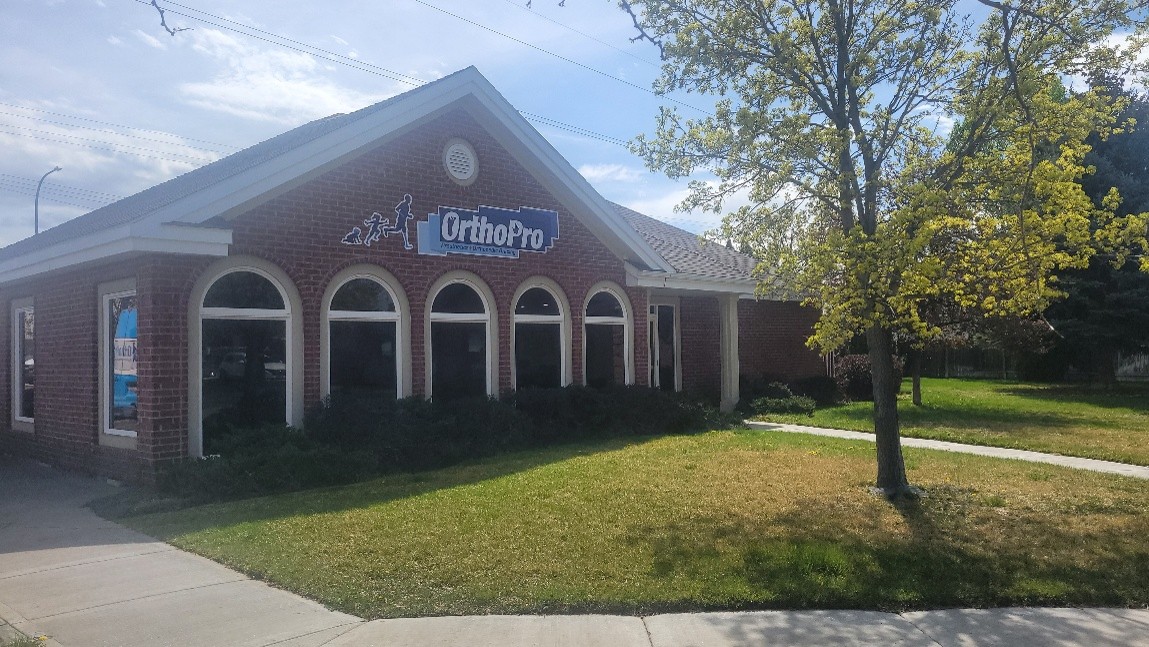 Brick office building with OrthoPro sign and arched windows next to a grassy lawn with a tree.