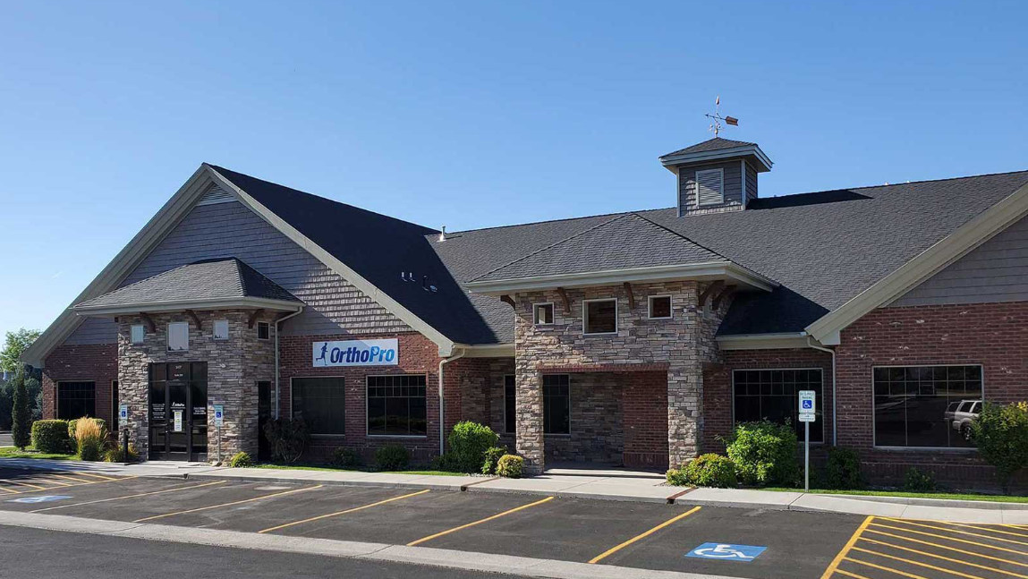 Modern brick and stone commercial building under clear blue sky with OrthoPro sign and empty parking spaces.