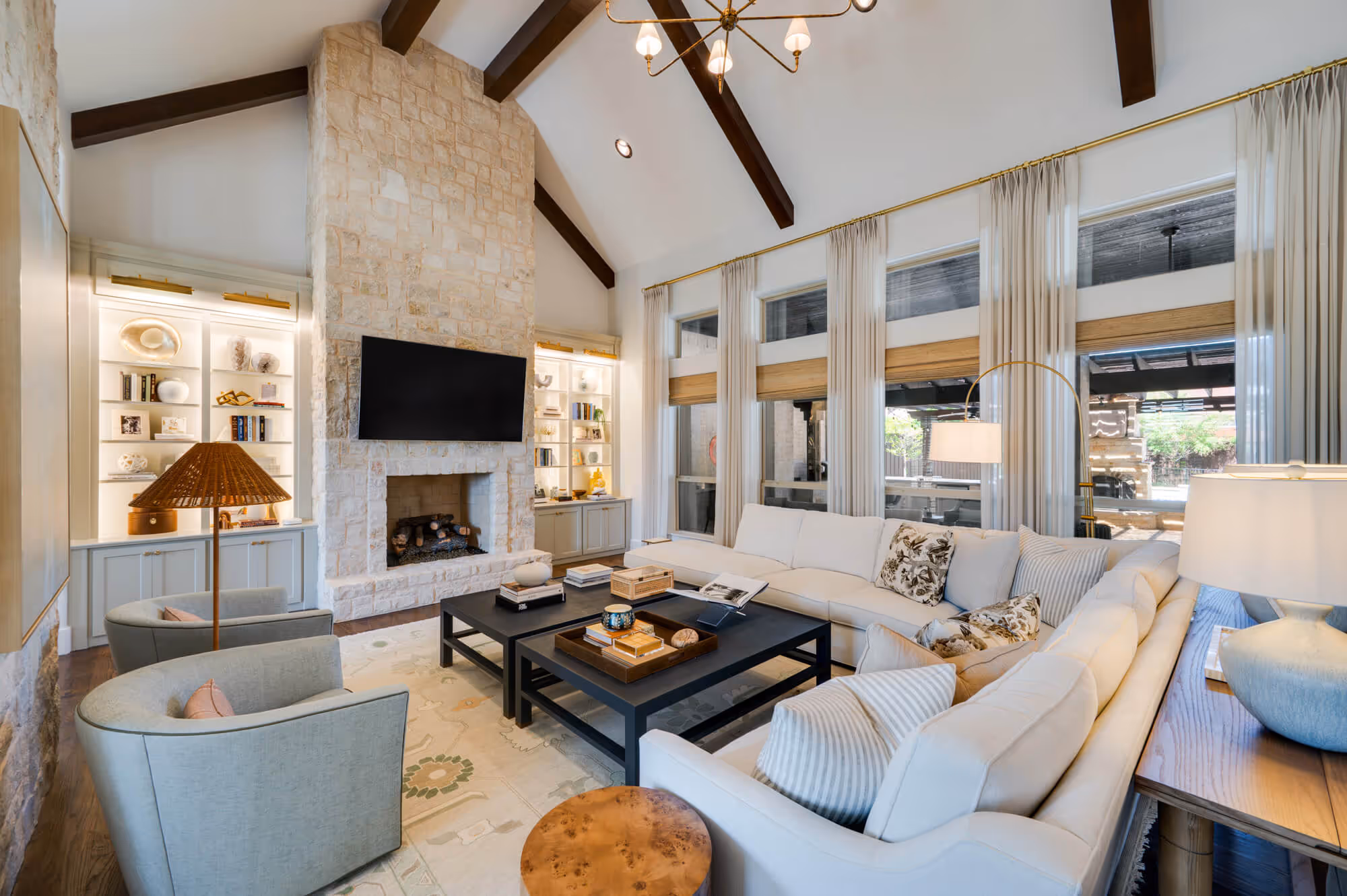 Spacious living room with vaulted ceiling, stone fireplace, large sectional sofa, two gray chairs, and black coffee tables.