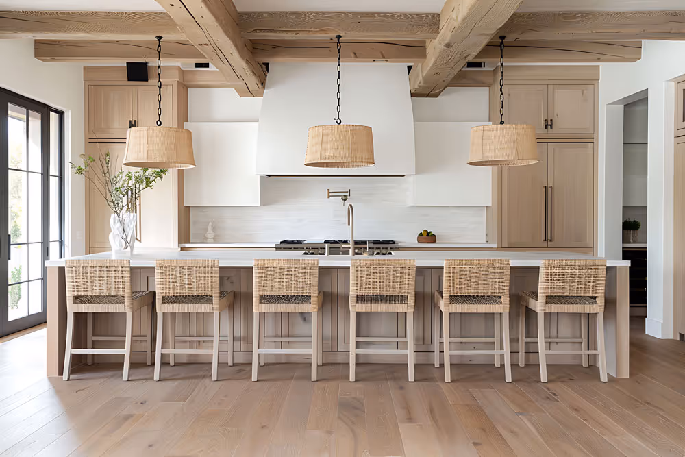 Spacious rustic kitchen with light wood beams, six wicker bar stools, white countertops, and three hanging woven pendant lights.