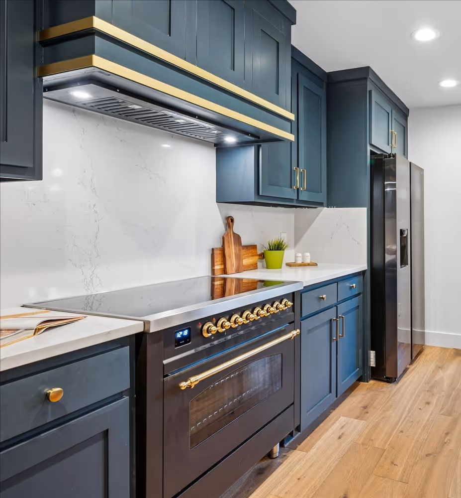 Modern kitchen with navy blue cabinets, a black stove with gold knobs, wooden floor, and stainless steel refrigerator.