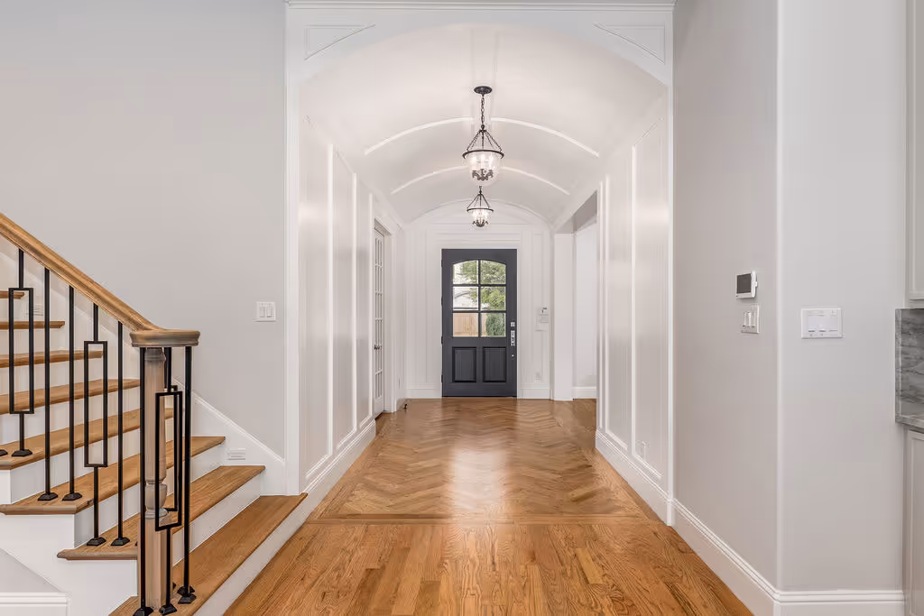 Modern hallway with arched ceiling, wooden herringbone floors, black front door, and staircase with wooden handrail and black metal balusters.