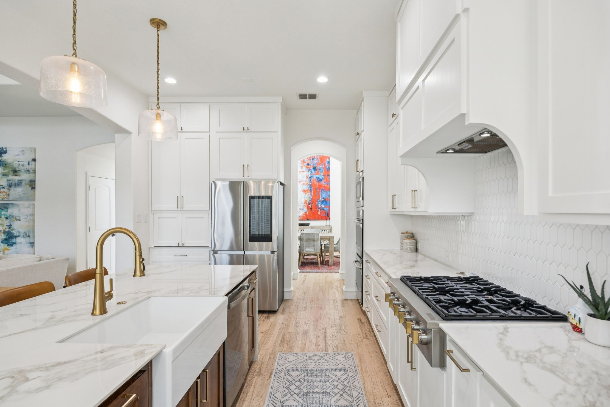 Modern kitchen with white cabinets, marble countertops, gold faucet, stainless steel appliances, and wooden floor.