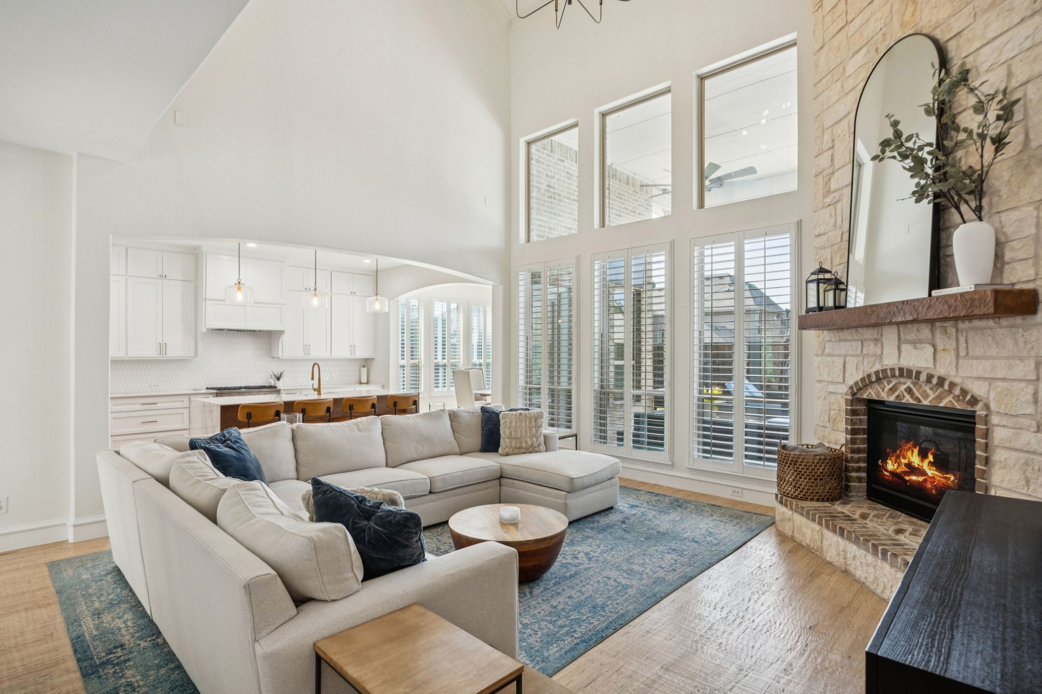 Bright open living room with beige sectional, blue rug, large windows, and stone fireplace with mirror.