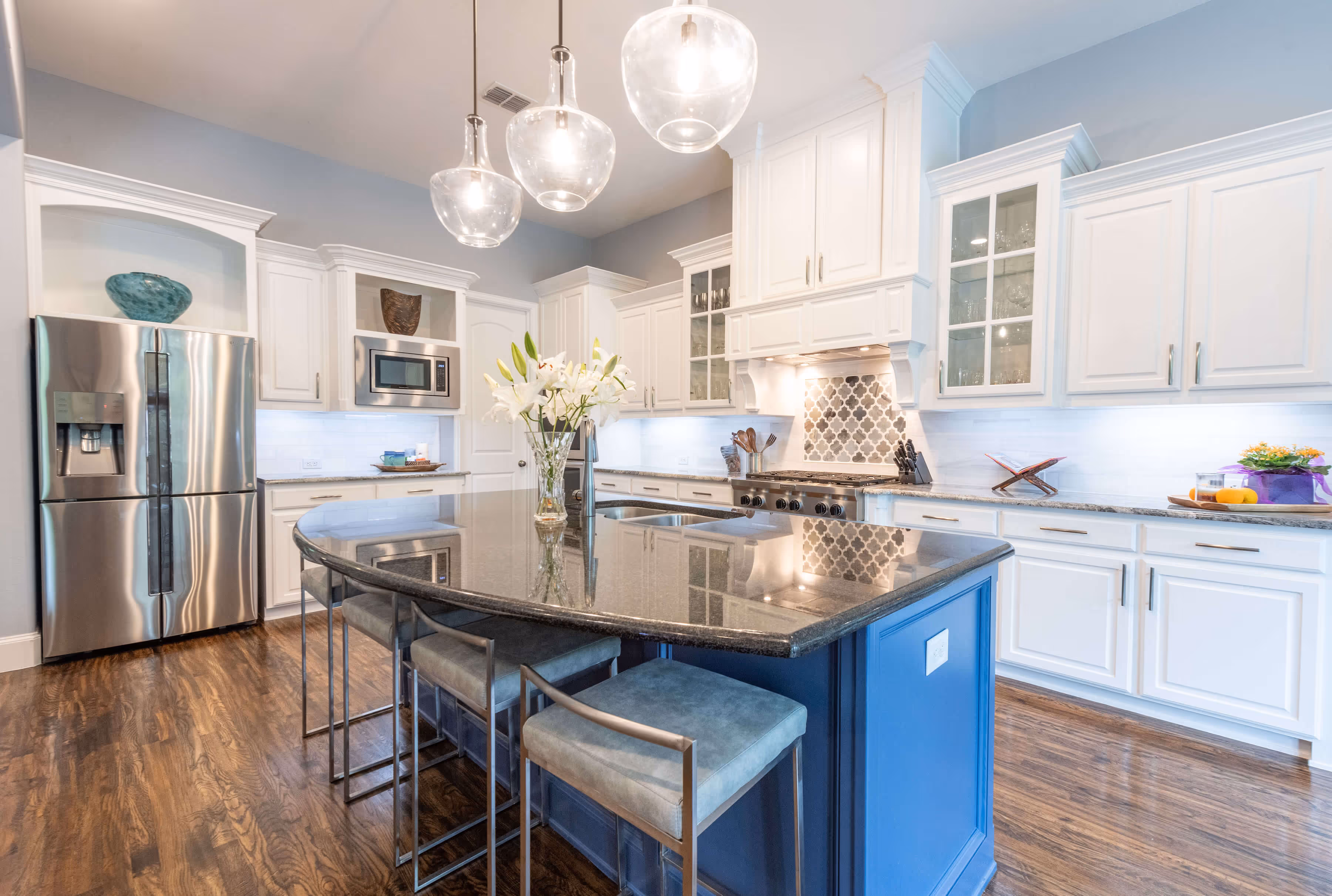 Modern kitchen with white cabinets, marble island, tan bar stools, and dining nook with large windows.