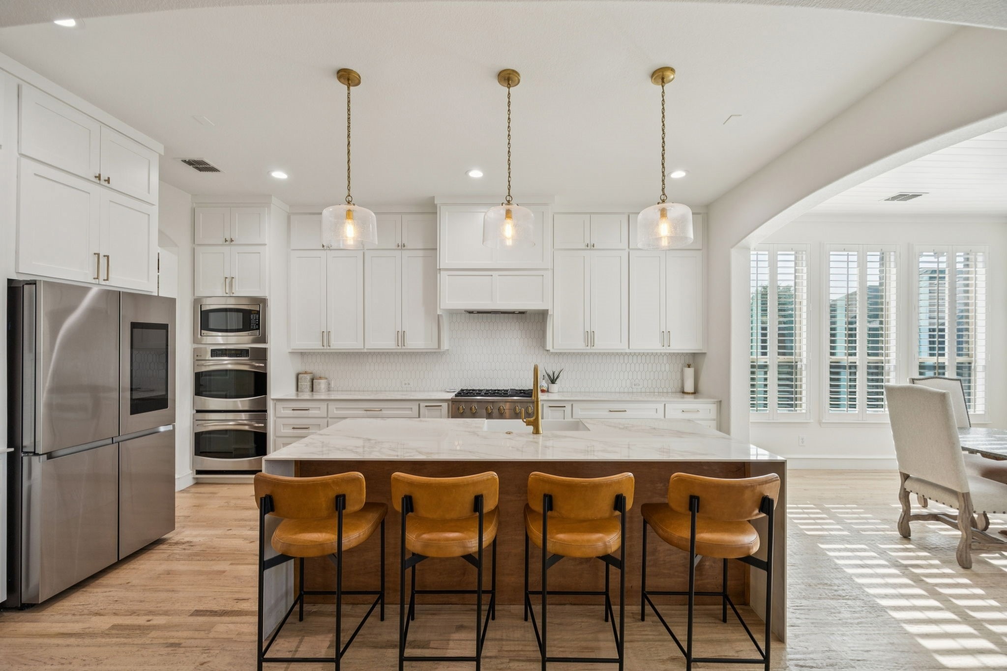 The fully renovated kitchen features custom white cabinetry, marble countertops, and a dramatic waterfall island accented by warm brass fixtures and leather bar seating.