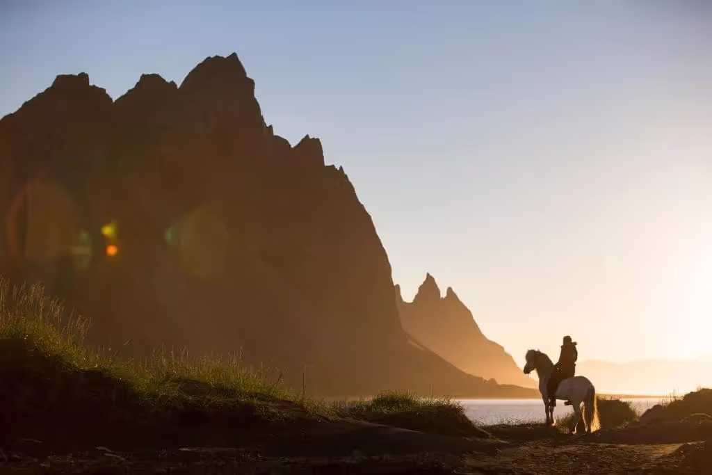 A person riding a horse with the sunlit peaks of Vestrahorn in the backdrop