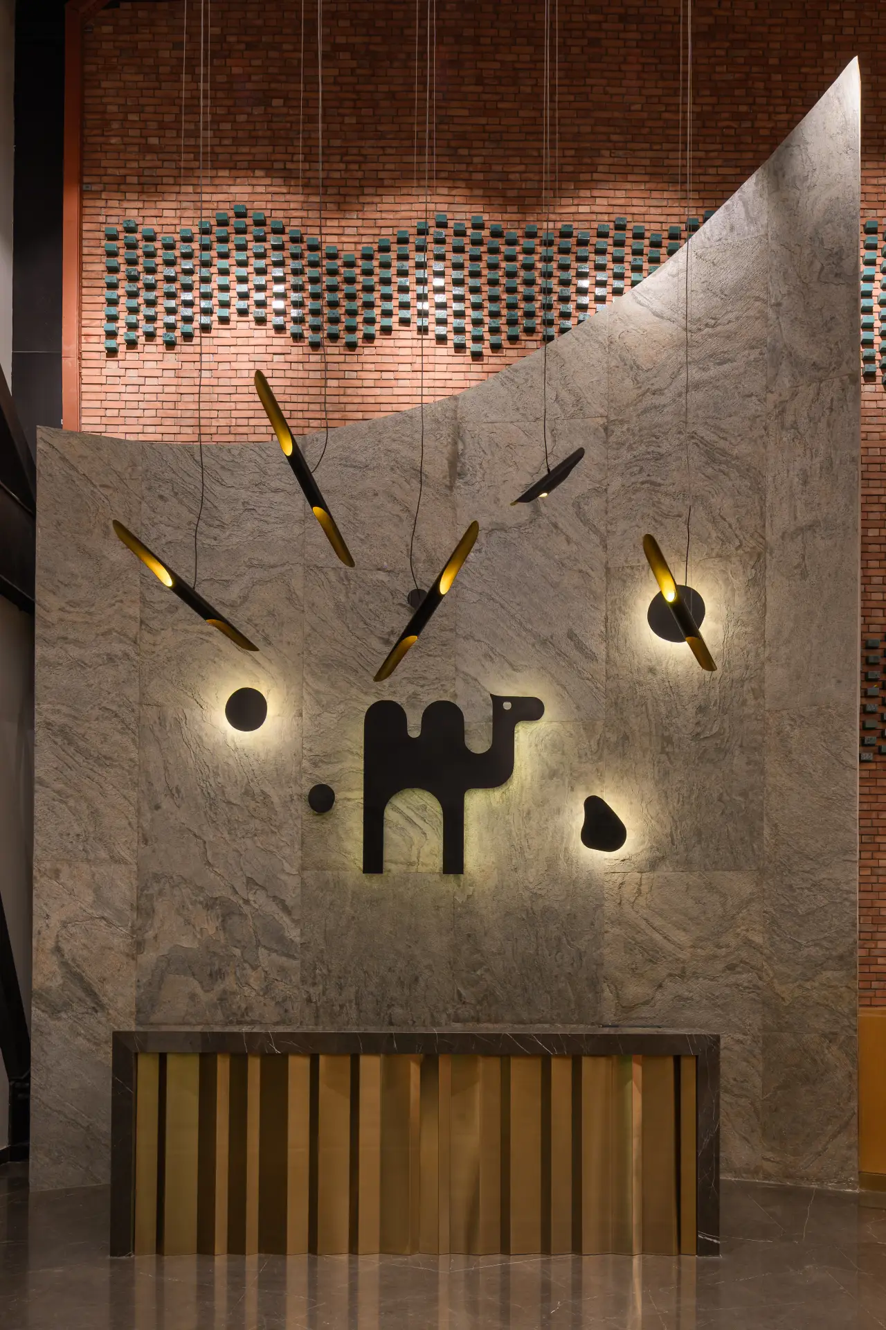 Reception area of Kamelizer Spaces District 5 branch in New Cairo, showcasing a contemporary design with a large illuminated camel logo, black accent wall, decorative chandeliers, and a geometric wooden reception desk.