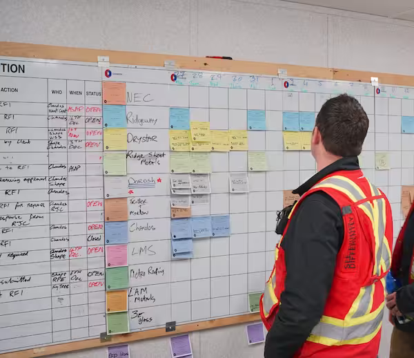 A person in a high-vis jacket collaboratively organize colorful sticky notes on a large wall calendar, creating a lean planning timeline