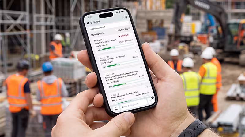 Person holding smartphone displaying construction project tasks with workers in safety vests on site.
