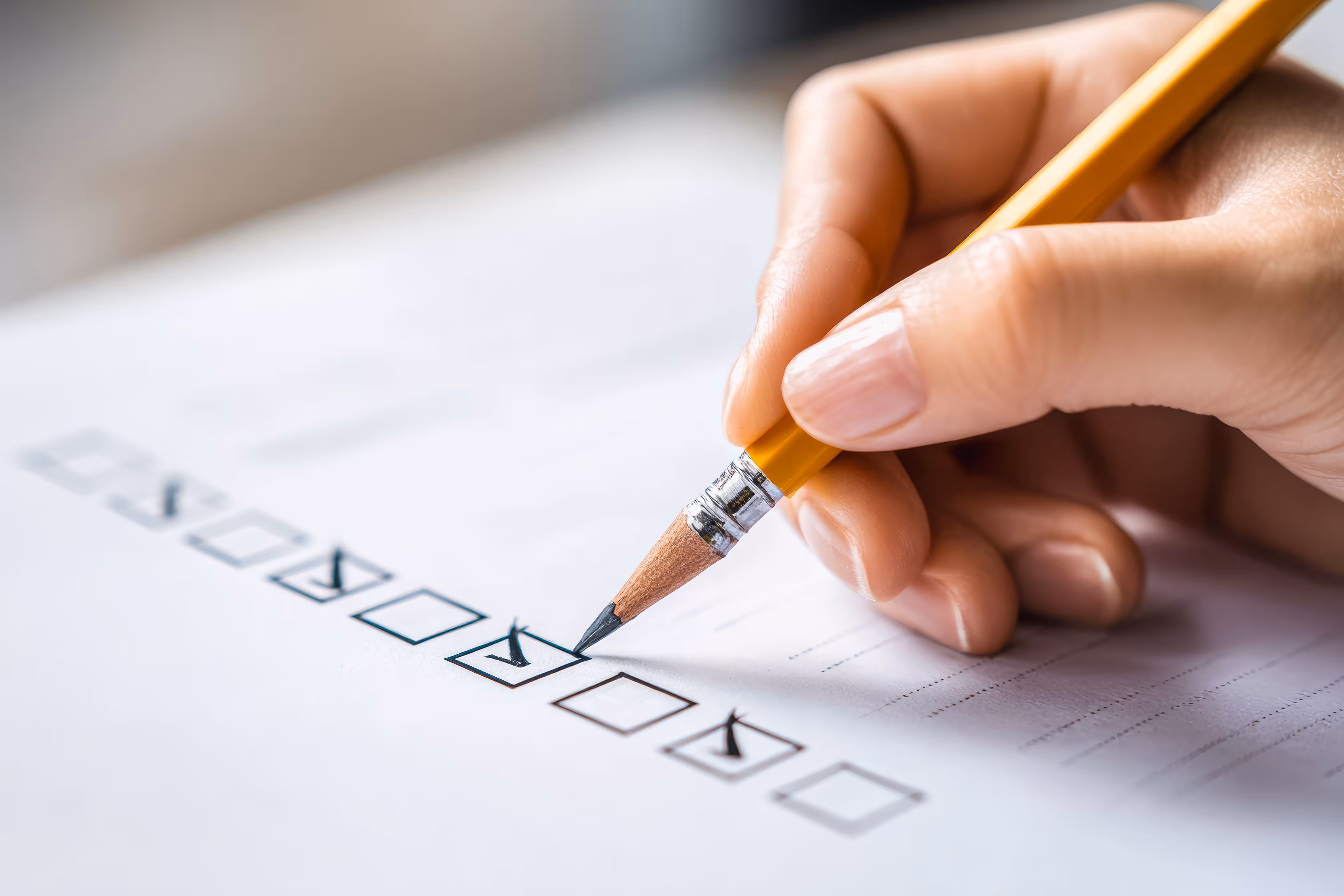 Close-up of a person's hand using a pencil to mark checkmarks in boxes on a printed document or survey.