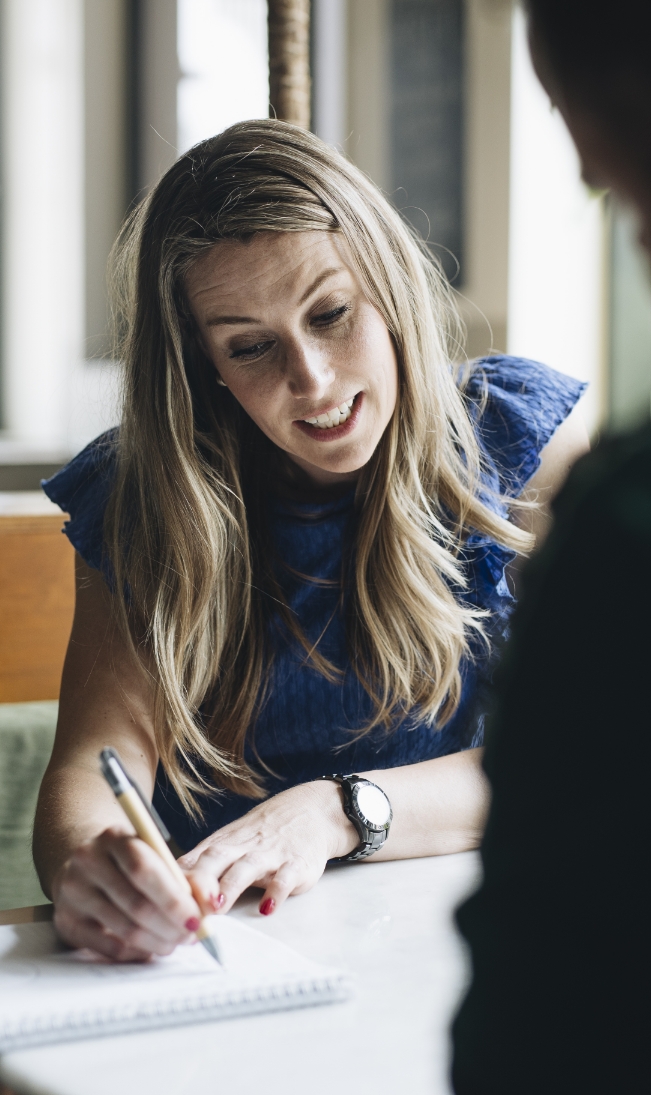 Trainer en coach Amanda Ronhaar van Toer de Werkvloer legt tijdens een coachingsgesprek wat uit dat op een schrijfblok staat.